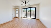 This contemporary two-story home in Phoenix, AZ offers four bedrooms and three bathrooms across two well-appointed floors. The main level features an open-concept kitchen and living area bathed in natural light from large black-framed windows. The kitchen is a standout, showcasing a spacious waterfall-edge island, crisp white upper cabinetry contrasted by warm wood-toned lower cabinets, stainless steel appliances including a gas range, and stylish pendant lighting overhead. Warm hardwood-style flooring flows seamlessly throughout the main living areas and continues upstairs. A convenient half bathroom on the main floor features matching wood cabinetry and gold hardware accents. The attached garage includes a modern panel door with horizontal windows. Upstairs, the generous primary bedroom offers a walk-in closet with built-in shelving and rods, plus a sliding glass door opening to an outdoor balcony with a ceiling fan. The primary bathroom is elegantly finished with a walk-in glass-enclosed shower, tiled surround, a wood vanity with white countertop, and gold fixtures. Secondary bedrooms are bright and airy, each with black-framed windows framing outdoor views. Three additional closets provide ample storage throughout this thoughtfully designed home.