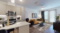 This single-story 1-bedroom residence at Avidity in Lutz, Florida, showcases a thoughtfully designed open-concept layout that seamlessly connects the kitchen, dining, and living areas. The kitchen is a standout feature, equipped with stainless steel appliances, sleek gray cabinetry, a white subway tile backsplash, and a granite-topped island with bar seating, illuminated by pendant lighting overhead. Wood-style flooring runs throughout the main living spaces, adding warmth and cohesion to the design.

The living area provides a comfortable and well-lit setting, with large windows dressed in grommet-panel curtains that allow natural light to filter in. The bedroom is generously proportioned, featuring large windows, wood-style flooring, and ample space for furnishings. The bathroom continues the contemporary aesthetic with gray cabinetry, granite countertops, a large mirror, and wood-style flooring. The overall color palette—neutral whites, warm grays, and natural wood tones—creates a clean, modern ambiance throughout the residence.