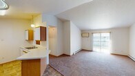 Located at 3570 42nd St S in Fargo, North Dakota, this single-floor unit offers a practical and comfortable layout designed for everyday living. The open-concept living and dining area features a combination of tile flooring near the entryway and kitchen, transitioning to plush carpeting throughout the living space. Vaulted ceilings in the living room lend a sense of openness, while a sliding glass door floods the room with natural light and provides access to an outdoor area. Baseboard heating is present throughout the unit, ensuring efficient climate control during Fargo's cold winters. The kitchen is equipped with warm-toned wood cabinetry, light countertops, a double stainless steel sink, a dishwasher, and a refrigerator. A pass-through window connects the kitchen to the living area, enhancing the open feel. A pendant light fixture adds a functional accent above the kitchen. The bedrooms are carpeted and well-sized, each featuring windows that allow natural light and views of the surrounding neighborhood. Closet storage is accessible from the bedroom area. The bathroom includes a full tub-shower combination with chrome fixtures, a vanity with storage, and light tile flooring. Textured ceilings are consistent throughout the unit, completing its clean, utilitarian aesthetic.
