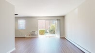 This single-floor residence offers a well-organized layout with a variety of functional spaces throughout. The living area is bright and open, featuring smooth hardwood-style flooring, neutral gray walls, and large sliding glass doors that frame views of surrounding greenery and brick exterior architecture. Baseboard heating runs along the perimeter, and a wall-mounted air conditioning unit provides climate control. Natural light fills the room generously through both the sliding doors and an additional side window.

A narrow, hardwood-floored entry hallway leads from the front door into the main living spaces, providing a clean transition into the unit. The kitchen features rich, dark mahogany cabinetry with brushed nickel hardware, white quartz countertops, a stainless steel undermount sink, and a marble-style subway tile backsplash, creating a polished, contemporary look alongside warm wood-tone flooring.

The bedrooms are carpeted with neutral tones and include ceiling fans with light fixtures. Each room offers closet storage, with one bedroom featuring a walk-in closet and another with a bifold-door closet. Both rooms benefit from natural light and direct access to adjoining spaces.

The bathroom is finished with light tile flooring, a white soaking tub and shower combo, a dark-cabinet vanity with a white countertop, and a window allowing natural light.