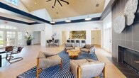 Located at 1000 Park Place Ave in Morrisville, NC, this thoughtfully designed single-floor community space offers a polished and inviting atmosphere throughout. The entry hallway greets visitors with light hardwood flooring, tall ceilings accented by bold navy trim, arched transom windows, and French doors that flood the space with natural light and provide views of the surrounding landscaped exterior.

The reception area features a dramatic coffered ceiling with layered navy and white detailing, light wood floors, wall-mounted display screen, and a warm mid-century modern credenza — creating a professional yet welcoming first impression.

The expansive living room is the centerpiece of the space, boasting soaring vaulted ceilings with a ceiling fan, shiplap accent walls, and a built-in wet bar with open shelving. Comfortable tufted seating arranged around a wood coffee table invites gathering, while a floor-to-ceiling tiled fireplace with direct outdoor access adds warmth and character. Large windows throughout ensure ample natural light.

A private meeting room enclosed by frosted glass doors offers an intimate setting with textured blue-grey wallcovering, patterned carpet, and contemporary furnishings — ideal for focused conversations. A full bathroom completes the layout, rounding out this versatile and elegantly finished community space.