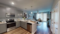 This single-floor residence is thoughtfully designed with a cohesive, modern aesthetic that flows seamlessly from room to room. The open-concept layout connects the kitchen and living area, creating a welcoming, functional space ideal for everyday living and entertaining.

The kitchen is a standout feature, outfitted with gray shaker-style cabinetry extending to the ceiling, white quartz countertops, a classic subway tile backsplash, and a full suite of stainless steel appliances including a range, over-the-range microwave, dishwasher, and refrigerator. A peninsula with an undermount sink and pendant lighting above bridges the kitchen to the living area, enhancing the open feel.

The living room benefits from large windows dressed with blinds and sheer curtains, allowing generous natural light to fill the space. Wood-look flooring runs throughout the main living areas, while a ceiling fan adds both style and practicality.

The bedrooms are carpeted for comfort and receive ample natural light through large windows. Each room offers access to closet space and connects to the bathroom, which features wood-look vinyl flooring, a gray vanity with white countertop, and a full tub-shower combination with a curtain enclosure.