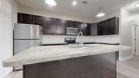 Located at 3400 Club Way Ct in Powell, Ohio, this two-story home offers four bedrooms, two full bathrooms, and a thoughtfully designed layout spread across two floors. The main floor comprises the majority of the living space, featuring an open-concept kitchen and living area with light wood-tone flooring throughout. The kitchen is outfitted with rich dark cabinetry, light stone-finish countertops, a large island with a built-in sink, and a full suite of stainless steel appliances including a refrigerator, range, microwave, and dishwasher. Pendant lighting and access to outdoor views through a sliding glass door add brightness and character to the space. A full bathroom on the main floor features dark vanity cabinetry and a tub-shower combo. A dedicated laundry room with a full-size washer and dryer provides added convenience. The upper floor hosts additional bedrooms, including a generously sized primary bedroom with a walk-in closet equipped with wire shelving. Secondary bedrooms feature plush carpeting and natural light from large windows. A spacious walk-in closet with wire rack storage and a well-appointed shared bathroom with a dark vanity complete the upper level. Neutral tones and clean finishes throughout create a cohesive, move-in-ready feel.