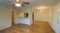 This single-floor space showcases a thoughtfully designed open-concept layout that promotes a seamless flow between the living and kitchen areas. Rich, warm-toned hardwood flooring spans the main living space, adding depth and character throughout. A ceiling fan with a light fixture keeps the living area comfortable, while a pendant light provides a welcoming focal point over the adjoining dining or sitting area.

The kitchen is defined by a pass-through counter finished with granite-style countertops, creating an ideal space for casual dining or entertaining. Stainless steel appliances, including a refrigerator, oven range, and built-in microwave, lend the kitchen a modern, polished look. Warm wood cabinetry provides ample storage and complements the overall color palette of the space. Visible ventilation features throughout suggest a well-maintained HVAC system.

The neutral, light-toned walls create a bright and airy ambiance, making the space feel open and versatile. The layout allows for flexible furniture arrangements, accommodating a variety of living styles. Overall, this space combines practical functionality with clean, contemporary design elements to create a comfortable and inviting environment.