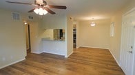 This single-floor space showcases a thoughtfully designed open-concept layout that promotes a seamless flow between the living and kitchen areas. Rich, warm-toned hardwood flooring spans the main living space, adding depth and character throughout. A ceiling fan with a light fixture keeps the living area comfortable, while a pendant light provides a welcoming focal point over the adjoining dining or sitting area.

The kitchen is defined by a pass-through counter finished with granite-style countertops, creating an ideal space for casual dining or entertaining. Stainless steel appliances, including a refrigerator, oven range, and built-in microwave, lend the kitchen a modern, polished look. Warm wood cabinetry provides ample storage and complements the overall color palette of the space. Visible ventilation features throughout suggest a well-maintained HVAC system.

The neutral, light-toned walls create a bright and airy ambiance, making the space feel open and versatile. The layout allows for flexible furniture arrangements, accommodating a variety of living styles. Overall, this space combines practical functionality with clean, contemporary design elements to create a comfortable and inviting environment.