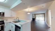 This single-floor residence is designed with a cohesive, modern aesthetic that balances functionality and comfort. The open-concept layout connects the kitchen and living area seamlessly, anchored by rich, dark hardwood flooring that extends throughout the main living spaces.

The kitchen is well-appointed with white shaker-style cabinetry, light countertops, and a classic subway tile backsplash. Stainless steel appliances—including a gas range, built-in microwave, refrigerator with ice dispenser, and dishwasher—offer a complete cooking suite. A peninsula with a double sink and breakfast bar separates the kitchen from the adjoining dining and living areas. A pendant light fixture overhead adds a refined finishing touch.

The living area is spacious and open, featuring a fireplace framed by a clean white mantle and large sliding glass doors that flood the space with natural light and provide access to an outdoor area. A bedroom features plush carpeting and its own sliding glass door, further enhancing the connection to the outdoors.

The bathroom is finished in a clean, minimal style with a pedestal sink, a large mirror, and contemporary vanity lighting above. Dark hardwood flooring continues here, maintaining visual consistency throughout the unit.