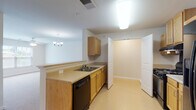 This single-floor unit is designed with a practical, open layout that connects the kitchen and living area seamlessly. The kitchen is well-equipped, featuring light wood cabinetry, light-toned countertops, a double sink, a black dishwasher, a gas range, and a black stainless refrigerator. Vinyl flooring runs throughout the kitchen, providing easy maintenance. A raised peninsula counter separates the kitchen from the adjoining living space, which is finished with neutral wall-to-wall carpet and illuminated by a ceiling fan with integrated lighting and a decorative chandelier. A window along one wall of the living area allows natural light to enter and offers an exterior view.

The bedroom areas continue the carpeted flooring and include panel-style closet doors that open to storage spaces with built-in shelving rods. The bathroom features vinyl flooring, an oak vanity with a single sink and light-toned countertop, a wall-mounted mirror, a chandelier-style light fixture, and a full-size tub and shower combination. Throughout the unit, white trim and neutral wall tones create a clean, cohesive aesthetic. The layout is efficient and well-organized, offering functional living spaces across a single level.