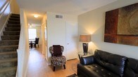 Located on Spring Hill Avenue in Mobile, Alabama, this two-story property offers a practical and comfortable layout designed for everyday living. The living area sets a welcoming tone with warm hardwood-style flooring that extends throughout the main level, creating a cohesive and inviting atmosphere. Neutral-toned walls provide a versatile backdrop, while ceiling-mounted lighting and a floor lamp contribute to a well-lit environment. The living space accommodates a relaxed seating arrangement, with a hallway leading further into the home, offering a sense of depth and connectivity between rooms. A glimpse of the dining area is visible toward the rear, suggesting an open and functional flow between living and dining spaces. Overhead HVAC vents indicate a central climate control system throughout. The two-floor layout provides natural separation between living and private spaces, making the property well-suited for a variety of occupants. Overall, the space presents a straightforward, clean interior with warm finishes and a layout that balances openness with defined functional areas.