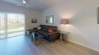 This two-floor residence offers a thoughtfully designed layout with a clean, contemporary aesthetic throughout. The kitchen is a functional highlight, featuring dark wood cabinetry, granite-style countertops, light wood-look tile flooring, a double stainless steel sink, and white appliances including a range and built-in microwave. A breakfast bar provides additional counter space and connects the kitchen seamlessly to the living and dining areas. The living room is warm and inviting, featuring light hardwood-style flooring, a ceiling fan, and access to an outdoor area through a glass door that fills the space with natural light. Multiple bedrooms are finished with plush carpeting and windows dressed with vertical blinds, offering comfort and ample natural light. Each bedroom provides generous space for furnishings. The bathrooms are well-appointed with wood-look flooring, granite-style vanity countertops, and clean white cabinetry, delivering a polished, modern look. The consistent use of neutral tones—whites, grays, and warm beiges—throughout the space creates a cohesive and airy atmosphere. The two-floor layout, as revealed in the dollhouse view, provides a practical and organized living environment suitable for a variety of lifestyles.