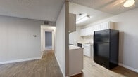 Located at 300 Riverwood Ln in Roswell, GA, this single-floor, two-bedroom, one-bathroom residence offers a functional and straightforward layout across a comfortable footprint. The living room serves as the central gathering space, featuring rich wood-look flooring, neutral gray walls, a ceiling fan, and a sliding glass door that fills the room with natural light and provides access to the outdoors. A central hallway connects the main living areas to the private quarters, maintaining a clear and efficient flow throughout the home. The galley-style kitchen is equipped with white cabinetry, light countertops, a black refrigerator, a range, and a dishwasher, all set on light wood-look flooring. A half-wall partition separates the kitchen from the hallway, adding a sense of openness. Both bedrooms are carpeted and finished in soft neutral tones, with the primary bedroom offering a generous footprint, a closet, and a window that brings in natural light. The full bathroom includes a combined tub and shower, a white vanity with storage, and wood-look tile flooring. Textured ceilings are consistent throughout, and two closets provide practical storage solutions for everyday living.