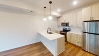 Located at 336 Second St NE in Minneapolis's vibrant Northeast neighborhood, this single-floor unit showcases a clean, contemporary design with a cohesive modern aesthetic throughout. Light-toned hardwood-style flooring flows consistently across the main living areas, anchoring the bright, neutral palette that defines the space.

The kitchen is a standout feature, offering light wood cabinetry, a white quartz peninsula with an undermount sink and matte black faucet, and stainless steel appliances including a range and over-the-range microwave. Globe pendant lights suspended above the peninsula add a warm, stylish focal point, while a classic subway tile backsplash and recessed lighting complete the polished look.

The bedroom is quiet and understated, with crisp white walls and a large black-framed window that invites natural light and frames views of the surrounding tree canopy — a particularly appealing feature in the warmer months.

The bathroom maintains the same modern sensibility, featuring large-format neutral floor tile, a full tub and shower combo finished with white subway tile, matte black fixtures and hardware, and a light wood vanity with ample storage. The overall layout, visible in the dollhouse view, is efficient and well-organized, making excellent use of the available footprint.