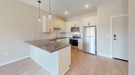 This well-designed 2-bedroom, 2-bathroom unit in Monticello, MN offers a thoughtful single-floor layout that maximizes comfort and functionality. The open-concept living and kitchen area serves as the heart of the home, where light wood-style flooring flows throughout. The kitchen is appointed with crisp white shaker cabinetry, dark countertops, a white subway tile backsplash, a full suite of stainless steel appliances — including a refrigerator, range, microwave, and dishwasher — and a central island with pendant lighting overhead. The adjacent living room is bright and airy, featuring a sliding glass door that opens directly onto a private balcony, filling the space with natural light and outdoor views. The primary bedroom offers a generous footprint with plush carpeting, a double-door closet, and direct access to a full bathroom. The second bedroom is equally comfortable, also carpeted, with easy access to a second full bathroom complete with a tub/shower combination and brushed nickel fixtures. Both bathrooms feature wood-look vinyl flooring. Warm neutral tones and clean white trim throughout create a cohesive, move-in-ready aesthetic suited for everyday living.