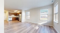 This two-floor residence offers a clean, modern aesthetic characterized by light hardwood flooring that flows consistently throughout both levels, crisp white walls, and abundant natural light streaming through multiple windows. The open-concept living and dining area on the main floor is spacious and airy, with large windows that provide views of the surrounding neighborhood and invite generous amounts of daylight into the space. A staircase connects the two floors, with the lower level also featuring a welcoming entryway.

The kitchen is well-equipped and functional, featuring warm-toned wood cabinetry with ample upper and lower storage, light countertops, and a full suite of stainless steel appliances including a refrigerator, electric range with overhead ventilation, and dishwasher. The hardwood flooring extends seamlessly into the kitchen, maintaining a cohesive look throughout the main living areas.

The upper floor hosts the bedrooms, each finished with the same light hardwood flooring and neutral wall tones. At least one bedroom includes a built-in closet with shelving. The bathroom features tile flooring, a wood vanity with a white countertop, a large mirror, and clean, understated finishes. Overall, the space presents a bright, move-in-ready environment with consistent, practical design details across both floors.
