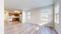 This two-floor residence offers a clean, modern aesthetic characterized by light hardwood flooring that flows consistently throughout both levels, crisp white walls, and abundant natural light streaming through multiple windows. The open-concept living and dining area on the main floor is spacious and airy, with large windows that provide views of the surrounding neighborhood and invite generous amounts of daylight into the space. A staircase connects the two floors, with the lower level also featuring a welcoming entryway.

The kitchen is well-equipped and functional, featuring warm-toned wood cabinetry with ample upper and lower storage, light countertops, and a full suite of stainless steel appliances including a refrigerator, electric range with overhead ventilation, and dishwasher. The hardwood flooring extends seamlessly into the kitchen, maintaining a cohesive look throughout the main living areas.

The upper floor hosts the bedrooms, each finished with the same light hardwood flooring and neutral wall tones. At least one bedroom includes a built-in closet with shelving. The bathroom features tile flooring, a wood vanity with a white countertop, a large mirror, and clean, understated finishes. Overall, the space presents a bright, move-in-ready environment with consistent, practical design details across both floors.