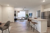 Located at 74401 Hovley Ln E in Palm Desert, California, this single-story residence offers a well-designed, open-concept layout with a clean, contemporary aesthetic. Light wood-style flooring flows seamlessly through the main living areas, anchoring a bright and cohesive interior.

The open-plan living, dining, and kitchen area forms the heart of the home. The kitchen is outfitted with white shaker cabinetry, light quartz countertops, a gray subway tile backsplash, stainless steel appliances including a gas range and built-in microwave, and a central island with bar seating—ideal for casual dining or entertaining. The dining area accommodates a table for four and features sliding door access to the exterior. The living area is generously proportioned with a ceiling fan overhead.

Multiple bedrooms provide comfortable private retreats, each featuring plush carpeting, ceiling fans, natural light from large windows with blinds, and ample closet space. One bedroom includes a walk-in closet and an en suite bathroom with wood-style flooring. A full bathroom with a tub-shower combination serves additional bedrooms.

A dedicated in-unit laundry room houses a full-size side-by-side washer and dryer with overhead shelving. Throughout the home, neutral wall tones and recessed lighting contribute to a calm, welcoming ambiance well-suited to the desert surroundings.