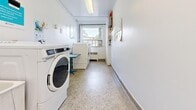 Located at 1710 Main St W in Hamilton, Ontario, this shared laundry facility is a compact, single-room space designed for efficient, practical use. The room is laid out in a rectangular configuration, with white walls and terrazzo flooring that give it a clean, utilitarian aesthetic. Fluorescent ceiling fixtures provide bright, even lighting throughout the space.

The room is equipped with multiple front-loading washing machines and dryers — identifiable as Maytag commercial units — positioned along the walls to maximize floor space. A utility sink with a faucet is available for pre-treatment or hand-washing needs, and a foldable table provides a convenient surface for sorting and folding laundry. A payment kiosk is present, indicating a card- or coin-operated system for machine use. Instructional signage is posted on the walls, offering guidance on machine operation and detergent usage.

Natural light enters through a large window on one wall, offering a view of the surrounding neighborhood. A baseboard heater beneath the window ensures comfortable temperatures year-round. The room is accessed through a solid door with a small window panel, and a second door provides additional access. Overall, the space is functional, well-maintained, and thoughtfully organized to serve the laundry needs of its users.
