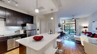 Located in Houston's desirable River Oaks area, this well-appointed one-bedroom, one-bathroom residence offers a thoughtfully designed single-level layout. The open-concept kitchen and living area serves as the heart of the home, anchored by a quartz-topped island with bar seating and pendant lighting overhead. The kitchen is outfitted with rich dark-espresso cabinetry, granite countertops, a tile mosaic backsplash, stainless steel appliances including a gas range, dishwasher, microwave, and refrigerator, and warm hardwood flooring that flows throughout the main living areas. The living room is bright and inviting, featuring a ceiling fan, large sliding glass door that floods the space with natural light and opens to an outdoor area. A dedicated office nook tucked within the unit features a granite-topped built-in desk and floating shelves, ideal for working from home. The bedroom offers plush carpeting, a generous window with natural views, and direct access to a walk-in closet with wire shelving. The bathroom is elegantly finished with large-format white tile, a soaking tub, a glass-enclosed walk-in shower, dual vanity with granite countertops, and bright overhead lighting. The overall ambiance is modern and polished, with clean lines and contemporary details throughout.