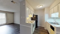 Located at 11500 Huebner Rd in San Antonio, Texas, this single-floor unit offers a well-organized layout designed for comfortable everyday living. The living area is finished with durable dark wood-style vinyl flooring and neutral gray walls, creating a clean, modern aesthetic throughout. Textured ceilings are consistent across the space, adding a classic residential character. A front entry door with vertical blinds allows for natural light control, while the open layout connects the living area seamlessly to the rest of the unit. The galley-style kitchen is efficiently arranged with white cabinetry, white countertops, and a full suite of appliances including an electric range, black refrigerator, and dishwasher. A built-in under-cabinet range hood and ample upper and lower cabinet storage make this kitchen highly functional. The bedroom features plush carpeting, a ceiling fan with light fixture, and a window fitted with blinds that allows natural light to filter in. The bathroom is finished with wood-style flooring consistent with the main living areas and includes a tiled tub/shower combination, toilet, and a vanity with countertop. The overall ambiance is clean, neutral, and move-in ready, offering a practical and comfortable living environment in the heart of San Antonio.