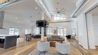 Located at 1681 Pampas Ln in Coeur d'Alene, Idaho, this single-floor community clubhouse is designed with a contemporary aesthetic and an open, airy layout. Soaring ceilings throughout the main gathering area create an impressive sense of volume, while exposed industrial-style ductwork adds a modern architectural contrast to the crisp white walls and warm wood-tone flooring.

The expansive main lounge is anchored by a dramatic floor-to-ceiling fireplace clad in dark slate tile, serving as a striking focal point. Multiple seating arrangements — including sofas, armchairs, and a coffee table — invite social interaction, while large windows along the perimeter flood the space with natural light and offer views of the surrounding community. An oversized ceiling fan and suspended flat-screen TV enhance the functionality of this gathering space.

The full kitchen features dark cabinetry with white quartz countertops, a large island with bar seating, a stainless steel range hood, and ample prep space — well-suited for community events and entertaining. A secondary kitchen or catering prep area provides additional counter and storage space.

Near the entrance, a shuffleboard table and a glass-enclosed office or workstation area add recreational and practical amenities. A fitness room is also accessible from the main corridor, rounding out this well-appointed community facility.