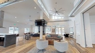 Located at 1681 Pampas Ln in Coeur d'Alene, Idaho, this single-floor community clubhouse is designed with a contemporary aesthetic and an open, airy layout. Soaring ceilings throughout the main gathering area create an impressive sense of volume, while exposed industrial-style ductwork adds a modern architectural contrast to the crisp white walls and warm wood-tone flooring.

The expansive main lounge is anchored by a dramatic floor-to-ceiling fireplace clad in dark slate tile, serving as a striking focal point. Multiple seating arrangements — including sofas, armchairs, and a coffee table — invite social interaction, while large windows along the perimeter flood the space with natural light and offer views of the surrounding community. An oversized ceiling fan and suspended flat-screen TV enhance the functionality of this gathering space.

The full kitchen features dark cabinetry with white quartz countertops, a large island with bar seating, a stainless steel range hood, and ample prep space — well-suited for community events and entertaining. A secondary kitchen or catering prep area provides additional counter and storage space.

Near the entrance, a shuffleboard table and a glass-enclosed office or workstation area add recreational and practical amenities. A fitness room is also accessible from the main corridor, rounding out this well-appointed community facility.