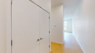 This single-floor unit presents a clean, contemporary design characterized by crisp white walls, light-toned hardwood flooring, and an open, airy layout throughout. The living and kitchen area is particularly notable for its generous proportions, anchored by large floor-to-ceiling windows that flood the space with natural light and offer views of the surrounding urban streetscape.

The kitchen is well-appointed with white shaker-style cabinetry, granite countertops, a stainless steel refrigerator, range, microwave, and dishwasher, all complemented by recessed track lighting overhead. The open connection between the kitchen and living area creates a seamless flow ideal for everyday living.

The bedrooms are comfortably sized, each featuring light hardwood floors, bright windows with exterior views, and white walls. At least one bedroom includes access to a dedicated walk-in closet with built-in rod storage. The unit contains two bathrooms: one featuring a full tub-shower combination with white tile surround and granite vanity, and a second with a walk-in shower stall. Both bathrooms maintain the unit's consistent clean, modern aesthetic with white cabinetry and coordinating finishes throughout.