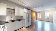Located at 45 Washington St in Haverhill, MA, this one-bedroom, one-bathroom unit blends industrial character with modern finishes. The open-plan living and kitchen area is anchored by a striking exposed brick accent wall, complemented by light hardwood flooring and track lighting throughout. Large windows flood the space with natural light and offer views of the surrounding streetscape.

The kitchen is well-appointed with white shaker cabinetry, dark countertops, a subway tile backsplash, and a full suite of Whirlpool appliances including a gas range, microwave, dishwasher, and a side-by-side refrigerator. The layout flows seamlessly into the living area, making the space feel open and functional.

The bedroom is carpeted and bright, featuring two large windows with black-framed trim that invite ample daylight. The bathroom is cleanly finished with white subway tile surrounding the tub/shower, a floating vanity, and tile flooring.

A dedicated laundry area houses a stacked Bosch washer and dryer, adding everyday convenience. Additional storage is provided by a hallway closet. The unit's overall design balances historic charm through its exposed brick with contemporary updates, creating a cohesive and practical living environment.