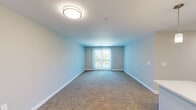 This single-floor residence offers a practical and well-organized layout across three bedrooms, two bathrooms, a dedicated closet, and a combined kitchen and living area. Neutral-toned walls and consistent white baseboards throughout create a clean, cohesive aesthetic, while plush carpeting covers the bedroom and living areas, contrasting with durable light wood-look flooring in the kitchen.

The living room is generously proportioned, featuring a flush-mount ceiling light and a sliding glass door fitted with vertical blinds that provides outdoor access and brings in natural light. The kitchen runs in a galley configuration, equipped with dark-stained cabinetry, light countertops, stainless steel appliances including a full-size refrigerator and range, and a single-basin sink.

The bedrooms vary in scale, with the primary bedroom offering a comfortable footprint. Several bedrooms feature sliding glass or standard windows fitted with blinds, ensuring natural light and privacy. A reach-in closet with wire shelving and hanging rods provides dedicated storage in one of the bedrooms.

The bathroom showcases hexagonal tile flooring, a walk-in shower with a white surround, a dark-stained vanity with a white countertop, and a mirror. The overall design is clean, modern, and move-in ready.
