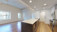 Located at 1220 Huron Rd E in Cleveland, Ohio, this modern single-floor unit offers a thoughtfully designed open-concept layout with contemporary finishes throughout. The living area is bright and spacious, featuring warm hardwood-style flooring, soaring ceilings with exposed beam detailing, and multiple windows that frame urban views of the surrounding cityscape.

The kitchen is a standout feature, showcasing a large center island with a white quartz countertop and built-in microwave drawer, complemented by sleek dark cabinetry. The full kitchen wall features white upper cabinets, a tile backsplash, stainless steel appliances including a range and refrigerator, and a range hood — all illuminated by recessed lighting above.

The bedroom is generously proportioned with vaulted ceiling elements, hardwood-style flooring, and a large window providing natural light and city views. It connects directly to a walk-in closet with built-in shelving.

The bathrooms are finished in a clean, neutral palette with large-format light tile flooring. One bathroom includes a soaking tub with a tiled surround and handheld showerhead, while another features a glass-enclosed shower. Both include floating vanities with white countertops and accessibility grab bars. An in-unit washer and dryer is also included.