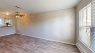 This two-story residence in Lynchburg, Virginia, offers a practical and well-organized layout spread across two levels. The main floor features an open-concept kitchen and living room finished with durable light-toned laminate wood flooring throughout. The living area is bright and airy, with natural light streaming through a large front-facing window that also provides an outdoor view. A staircase connects the main level to the upper floor. The kitchen is equipped with warm oak cabinetry, a granite-style countertop, a dark decorative tile backsplash, a white electric range, and a stainless steel sink — all functional elements designed for everyday use. A hallway on the main level leads to a dedicated laundry closet housing a stacked washer and dryer unit, adding significant convenience. The full bathroom features textured walls, a vanity with a mirror, and standard fixtures. Upstairs, the generously sized primary bedroom is carpeted in neutral tones, offering a comfortable and quiet retreat with a door for privacy and natural light from a window. The upper level also includes a hallway that connects the bedroom and bathroom. Throughout the home, a neutral color palette of warm grays and beiges creates a clean, move-in ready atmosphere.