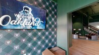 Located at 2801 Locust St in St. Louis, Missouri, this single-floor commercial space makes a strong first impression with its dramatic interior design. Deep forest green walls dominate throughout, creating a rich, immersive atmosphere that is both sophisticated and energetic. Light hardwood flooring stretches across the open layout, providing a warm contrast to the bold wall color and the exposed industrial ceiling above, which features visible structural beams and ductwork painted to match the green palette.

The main area is generously proportioned, offering an open, flexible floor plan well-suited for a variety of uses. A grand staircase with a dark wood handrail and wrought iron balusters serves as a striking architectural centerpiece, leading to upper levels. An elevator is also accessible, adding convenience.

The space is furnished with distinctive, eclectic seating — including curved metallic sofas and sculptural accent chairs — lending a contemporary, lounge-like character. Multiple flat-screen displays are mounted along one wall, ideal for digital signage or entertainment. Elegant wall sconces illuminate a clean white accent wall, adding a refined touch. Natural light filters in through glass-paned entry doors at one end, while recessed and track lighting illuminate the interior throughout. The overall ambiance is bold, modern, and highly curated.
