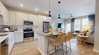 This thoughtfully designed 2-bedroom, 2-bathroom residence offers a seamless open-concept layout that connects the kitchen, dining, and living areas into one cohesive, welcoming space. The kitchen is a standout feature, showcasing crisp white cabinetry, a full suite of stainless steel appliances, a classic tile backsplash, and a center island with a dark countertop that doubles as a breakfast bar, complemented by stylish pendant lighting overhead. Light wood-style flooring flows throughout the main living areas, enhancing the bright, airy atmosphere. The living room is generously sized with large windows that invite ample natural light and a ceiling fan overhead. A private balcony extends from the living area, offering views of the surrounding community and outdoor grounds. Both bedrooms are carpeted and comfortably scaled, with the primary bedroom featuring a walk-in closet with built-in shelving. Each bathroom is finished with white cabinetry, quartz-style countertops, and wood-look flooring, with one bathroom offering a tiled tub-shower combination. A hallway and dedicated closet round out the functional layout of this well-organized, single-story residence.