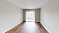 Located at 5700 Pleasant Ridge Rd in Knoxville, Tennessee, this one-bedroom, one-bathroom unit offers a well-organized, single-floor layout with wood-look flooring carried consistently throughout every room. The combined kitchen and living area forms the heart of the unit, with a sliding glass door flanked by vertical blinds opening to a private balcony that brings in natural light and outdoor views. The kitchen is outfitted with white cabinetry, granite-style countertops, a dishwasher, refrigerator, and an electric range, all set against a clean, neutral color palette. A textured ceiling adds a subtle design element to the living space. The bedroom is a comfortable size, featuring a window with outdoor views, two closets offering generous storage, and access to the hallway. The full bathroom includes a tub/shower combination with built-in corner shelving and chrome fixtures. Additional functional spaces include a dedicated utility room and a hallway connecting the rooms. Neutral gray walls, white trim, and warm wood-look floors create a cohesive, move-in-ready aesthetic throughout this practical and well-appointed Knoxville residence.