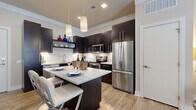 Located at 3600 Park East Dr in Beachwood, Ohio, this thoughtfully designed one-bedroom, one-bathroom residence offers a cohesive open-concept layout with modern finishes across every room. The kitchen is a standout feature, showcasing rich dark cabinetry, a classic white subway tile backsplash, stainless steel appliances, and a central island with a light stone countertop that doubles as a casual dining space with pendant lighting above. Wood-look flooring flows seamlessly from the kitchen into the open living area, which is bathed in natural light through multiple windows dressed with elegant sheer curtains. Crown molding adds a refined architectural touch to the living room. The bedroom is a comfortable retreat, carpeted for warmth, with a window providing natural light, direct access to a well-organized walk-in closet featuring built-in shelving and multiple hanging rods. The bathroom is finished with large-format tile flooring, a dark vanity with a marble-style countertop, and a full soaking tub with subway tile surround. Throughout the residence, neutral wall tones and consistent design elements create a clean, modern, and inviting ambiance.