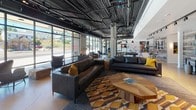 Located at 1521 Tacoma Ave S in Tacoma, Washington, this single-floor amenity space combines industrial design with contemporary finishes to create a dynamic, multi-functional environment. The reception area sets the tone immediately, featuring a bold reclaimed wood accent wall, a branded metal logo, black cabinetry, and industrial pendant lighting that together establish a cohesive modern aesthetic throughout the space.

The expansive main lounge is defined by its exposed ceiling with dark-painted ductwork and structural elements, large floor-to-ceiling grid windows that flood the interior with natural light and offer street-facing views, and stylish seating arrangements anchored by a geometric wood coffee table and patterned area rugs in warm amber and charcoal tones. A sleek, black double-sided fireplace serves as a striking architectural divider, adding warmth and visual interest while separating distinct zones within the space.

The entertainment area features a full-size billiards table centered beneath industrial pendant lights, complemented by reclaimed wood wall paneling and curated artwork. Adjacent to this, the well-equipped fitness center includes cardio machines, free weights, cable equipment, and mirrored walls that enhance the sense of space. Large windows connect the gym visually to an outdoor area, ensuring natural light throughout workouts.