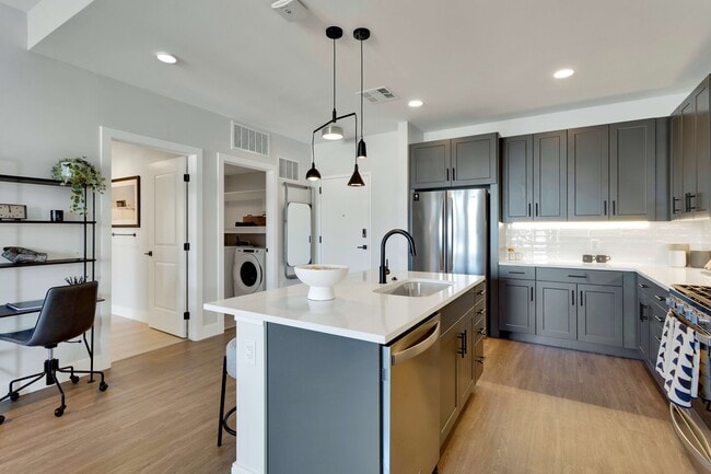 Modern kitchen with sleek dark cabinets, elegant pendant lighting, and a spacious island with integrated sink, offering a stylish workspace. - The Fitzgerald
