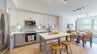 Located at 5400 Broken Sound Blvd NW in Boca Raton, Florida, this single-floor residence offers a thoughtfully designed open-concept layout that seamlessly connects the kitchen, dining, and living areas. The kitchen is outfitted with white upper cabinetry, gray lower cabinetry, stainless steel appliances, a mosaic tile backsplash, and a central island with bar seating — ideal for both cooking and casual dining. Light hardwood flooring flows throughout the main living areas, enhancing the bright, airy atmosphere created by large windows with views of lush Florida greenery.

The living room is generously proportioned, featuring a ceiling fan, ample natural light, and a relaxed coastal aesthetic with neutral tones and blue accents. The bedrooms are well-appointed, each offering carpeted flooring, large windows, and calming color palettes — one featuring a serene light blue accent wall and another showcasing a bold deep-blue feature wall with framed botanical artwork.

The primary bathroom is spa-like, featuring a dual-sink vanity with gray cabinetry, white quartz countertops, large-format tile flooring, a soaking tub, and a separate glass-enclosed walk-in shower with matte black fixtures. A dedicated in-unit laundry closet with a stacked washer and dryer adds everyday convenience.