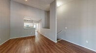 This two-story residence offers a thoughtfully arranged layout across two levels, with a mix of flooring materials that define each area. The main living area greets you with warm, wood-look vinyl plank flooring and soaring double-height ceilings that create an impressive sense of openness. A staircase connects the levels, with a half-wall detail at the landing that adds architectural interest to the space.

The galley-style kitchen is efficiently designed with white cabinetry, white tile flooring, a double-basin sink, and a full suite of white appliances including a refrigerator, electric range, microwave, and dishwasher. A raised breakfast bar separates the kitchen from the living area.

The bedroom features plush carpeting, a ceiling fan, and a sliding glass door that opens directly to a private outdoor patio area with fenced surroundings. Two full bathrooms serve the home — one featuring a tub-shower combination with white tile surround, and the other a walk-in shower — both with light tile flooring, white cabinetry, and ample storage. Hallway corridors with wood-look flooring connect the rooms seamlessly.

Completing the home is an attached single-car garage with an automatic opener, offering convenient and secure parking or additional storage space.