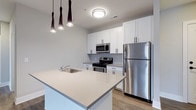 Located at 223 E Town St in the heart of Columbus, Ohio, this single-floor residence offers a clean, contemporary design throughout. The kitchen serves as a standout feature, showcasing crisp white shaker-style cabinetry that extends to the ceiling for ample storage, complemented by light quartz countertops and a large central island with a built-in sink — perfect for both meal preparation and casual dining. Stainless steel appliances, including a gas range, microwave, and full-size refrigerator, add a polished, modern aesthetic. Stylish pendant lighting with dark, tapered fixtures hangs above the island, creating a refined focal point that contrasts beautifully with the bright, neutral palette. The space is finished with warm wood-tone luxury vinyl plank flooring that flows seamlessly underfoot, contributing to the overall sense of cohesion and warmth. Flush ceiling lighting ensures the space remains well-lit, while the open-concept layout promotes an airy, connected feel. The design balances functionality with modern style, making it well-suited for those seeking a thoughtfully appointed residence in a vibrant urban Columbus location.