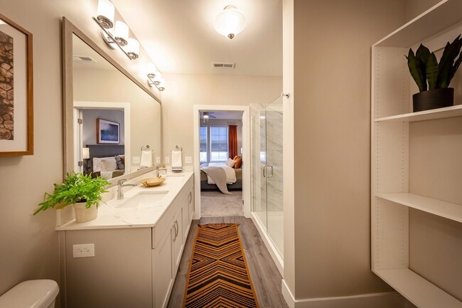 Modern apartment bathroom featuring elegant fixtures, a spacious vanity, glass-enclosed shower, and direct access to a private bedroom suite. - Madison at Greenwood