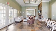 Located at Belmere Luxury Court in Houma, Louisiana, this elegantly designed single-floor space offers a seamless blend of comfort and functionality across its thoughtfully arranged rooms.

The centerpiece of the space is a spacious living room distinguished by soaring ceilings with decorative coffered detailing, warm sage-green walls, and rich slate tile flooring. A dramatic floor-to-ceiling stacked stone fireplace anchors the room, complemented by arched doorways framed with classic white columns that lead into the adjoining dining area. French doors flood the space with natural light and provide views of the outdoor pool area.

The dining room connects fluidly to the living space through the arched colonnade, offering additional seating and casual bar-height counter space along windowed walls that invite abundant natural light.

The kitchen is well-equipped with granite countertops, crisp white cabinetry, stainless steel appliances including a side-by-side refrigerator, double sink, and ample storage — all brightened by large windows overlooking the grounds.

A dedicated office features an extended granite-topped work surface accommodating multiple workstations, light tile flooring, and a glass-paneled door providing direct exterior access and natural light. Together, these spaces create a polished, welcoming environment suited for both productivity and leisure.