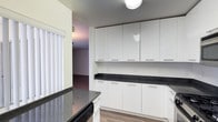 This single-floor residence features a clean, contemporary design with consistent wood-look flooring throughout. The kitchen is well-appointed with sleek white cabinetry extending from floor to ceiling, dark granite countertops, and a full suite of stainless steel appliances, including a gas range, over-the-range microwave, and a French door refrigerator. A peninsula provides additional prep space and separates the kitchen from the adjoining living and dining areas. The open living space is highlighted by a fireplace with a simple white mantel and connects seamlessly to a dining area illuminated by a pendant light fixture, with sliding glass doors fitted with vertical blinds drawing in natural light. A dedicated in-unit laundry closet is conveniently accessible from the main living area. The bedroom offers ample storage through a wide mirrored sliding-door closet that also enhances the sense of space. The bathroom features white cabinetry with dark granite countertops, a well-lit vanity mirror, and a separate water closet housing a soaking tub with a glass sliding shower enclosure. The overall palette of whites and neutrals gives the space a bright, cohesive feel.