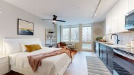 This well-appointed studio offers a smart, open-concept layout that maximizes every square foot across its single floor. The main living area is bright and inviting, anchored by a wall of large windows that flood the space with natural light and offer views of the surrounding neighborhood. Light wood-tone flooring runs throughout, complementing the neutral color palette and creating a warm, cohesive ambiance. A ceiling fan with integrated lighting adds both function and style to the living and sleeping area, which also features a spacious closet with built-in shelving for ample storage.

The kitchen is a standout feature, showcasing a striking herringbone tile backsplash, two-tone cabinetry with dark lower cabinets and crisp white uppers, light quartz countertops, and a full suite of stainless steel appliances including a refrigerator, range, microwave, and dishwasher. Track lighting overhead ensures excellent task illumination throughout.

The bathroom is clean and functional, featuring wood-look tile flooring, a white vanity with quartz countertop, a framed mirror, matte black fixtures, and a full tub-shower combination. A dedicated in-unit laundry closet with a stacked washer and dryer adds significant everyday convenience to this efficiently designed space.