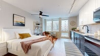 This well-appointed studio offers a smart, open-concept layout that maximizes every square foot across its single floor. The main living area is bright and inviting, anchored by a wall of large windows that flood the space with natural light and offer views of the surrounding neighborhood. Light wood-tone flooring runs throughout, complementing the neutral color palette and creating a warm, cohesive ambiance. A ceiling fan with integrated lighting adds both function and style to the living and sleeping area, which also features a spacious closet with built-in shelving for ample storage.

The kitchen is a standout feature, showcasing a striking herringbone tile backsplash, two-tone cabinetry with dark lower cabinets and crisp white uppers, light quartz countertops, and a full suite of stainless steel appliances including a refrigerator, range, microwave, and dishwasher. Track lighting overhead ensures excellent task illumination throughout.

The bathroom is clean and functional, featuring wood-look tile flooring, a white vanity with quartz countertop, a framed mirror, matte black fixtures, and a full tub-shower combination. A dedicated in-unit laundry closet with a stacked washer and dryer adds significant everyday convenience to this efficiently designed space.