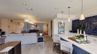 This thoughtfully designed single-floor amenity space offers a cohesive blend of modern aesthetics and practical functionality. The open-concept lounge and kitchen area serves as the heart of the space, where a striking deep-blue subway tile backsplash commands attention behind crisp white cabinetry and a light-toned breakfast bar. Pendant lighting in brushed gold finishes hangs above bar-height seating, while contemporary artwork adorns the walls. Large-format tile flooring flows seamlessly throughout, connecting each area with continuity and style. The lounge zone is furnished with comfortable sofas and accent chairs arranged around wooden coffee tables, all beneath elegant crystal chandelier fixtures. A textured stone accent wall frames a mounted flat-screen display, adding architectural depth to the gathering area. Adjacent to the lounge, a business center provides dedicated workstations equipped with computers, offering a productive environment for residents. The fitness room is well-appointed with cardio machines including treadmills and an elliptical, along with a full dumbbell rack and wall-to-wall mirrors. A separate leasing or meeting office features floor-to-ceiling windows that invite generous natural light and offer views of the surrounding landscape, creating a bright and welcoming reception environment. Colorful abstract artwork throughout adds a vibrant, curated character to the entire space.