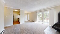 This single-floor residence offers a thoughtfully laid-out living space with a warm, neutral color palette throughout. The generously sized living room is a standout feature, anchored by a striking freestanding black wood-burning stove set against a brick accent wall. Large sliding glass doors flood the space with natural light and open onto a private balcony overlooking a lush, tree-lined outdoor setting. Plush carpeting extends across the living area, complemented by tile flooring beneath the stove and entryway. Crown molding and textured ceilings add a classic finishing touch throughout.

The galley-style kitchen is efficiently designed, featuring white cabinetry, warm countertops, wood-look flooring, and a full suite of black appliances including a refrigerator, dishwasher, and range. A window provides natural light to the cooking space.

The bedrooms are well-proportioned, each fitted with plush carpeting, crown molding, and baseboard heating. At least one bedroom includes a double-door closet for ample storage. The entry area features durable tile flooring, a wall-mounted HVAC unit, and access to a closet, providing practical convenience from the moment you step inside.