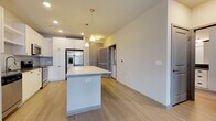 Located in Sandy Springs, GA (30328), this modern single-floor residence offers a thoughtfully designed open-concept layout with clean finishes throughout. The kitchen serves as the centerpiece of the living area, showcasing white shaker-style cabinetry that extends to the ceiling, a subway tile backsplash, dark quartz countertops, and a suite of stainless steel appliances including a French door refrigerator with ice maker, electric range, over-the-range microwave, and dishwasher. A generous central island with a quartz countertop provides additional prep space and built-in electrical outlets, illuminated by stylish pendant lighting above. Light-toned luxury vinyl plank flooring flows throughout the main living areas, complementing the neutral color palette. The living area benefits from abundant natural light through French doors with transom windows that open to a private balcony with views of surrounding greenery. The bedroom features plush carpeting and a well-sized window that brings in natural light. The bathroom is outfitted with white cabinetry, dark countertops, a soaking tub with tiled surround, and direct access to a walk-in closet with built-in shelving. Recessed lighting and pendant fixtures throughout enhance the bright, contemporary ambiance of this well-appointed Sandy Springs residence.