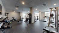 Located at 165 Belmont Ave in Belleville, NJ, this fitness center offers a comprehensive and well-organized workout facility spread across a single floor. The space is designed with functionality in mind, featuring a durable rubber flooring throughout that provides both safety and comfort during exercise.

The facility is divided into distinct workout zones. The main area houses a wide array of cardio equipment, including treadmills, elliptical machines, and stationary cycling bikes, many of which are positioned near large windows that flood the space with natural light and offer views of the surrounding neighborhood. A dedicated strength training section features a multi-station cable machine, a Smith machine with Olympic weights, a weight bench, and a rack of dumbbells, catering to a full range of resistance training needs.

An additional section includes medicine balls, resistance bands, and wall-mounted flat-screen TVs, creating an engaging environment for functional and group-style workouts. A ceiling fan aids in air circulation throughout this area.

The overall aesthetic is clean and modern, with neutral-toned walls, a drop-panel ceiling with recessed lighting, and a well-maintained interior. The layout is spacious, allowing for comfortable movement between equipment. Structural columns are integrated thoughtfully into the floor plan without disrupting the flow of the space.
