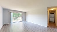 This single-floor residence offers a practical and comfortable layout with two bedrooms, two bathrooms, a kitchen, and a connecting hallway. The living area is bright and open, featuring light gray luxury vinyl plank flooring and clean white walls that create an airy atmosphere. A full-width sliding glass door opens to a private balcony, flooding the space with natural light and offering peaceful views of surrounding greenery.

The kitchen is outfitted with light gray shaker-style cabinetry, white countertops, and a full suite of stainless steel appliances, including a gas range, microwave, dishwasher, and refrigerator. The light hardwood-style flooring carries through the kitchen, complementing its clean, modern aesthetic.

Both bedrooms feature plush carpet flooring and windows with tree-lined views. The spacious primary bedroom includes two sets of built-in closets with shelving, providing generous storage. The second bedroom also offers closet space and is well-sized for flexible use.

The two bathrooms are finished in a clean, neutral palette. One features white subway tile surrounding the tub and shower combination, while the second offers a similarly configured tub-shower with tile flooring. Both are equipped with chrome fixtures throughout.