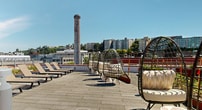 This innovative rooftop space in Seattle seamlessly blends urban agriculture with leisure amenities. The area features an extensive array of raised garden beds, showcasing a variety of vegetables and herbs in neatly organized rows. These planters, constructed from durable materials, are interspersed throughout the space, creating a productive green oasis.

The rooftop's design incorporates multiple seating areas, including comfortable lounge chairs, hanging egg chairs, and communal tables, providing diverse options for relaxation and socializing. A striking red structure houses indoor facilities, likely including a lounge or event space, with large windows offering views of the surrounding cityscape.

Landscaping elements add visual interest and ecological value. Ornamental grasses, flowering plants, and shrubs are strategically placed, creating a naturalistic feel. A notable feature is the stone pathway winding through portions of the garden, adding an organic touch to the urban setting.

The space offers breathtaking panoramic views of Seattle's skyline, with prominent skyscrapers and ongoing construction visible, highlighting the city's dynamic growth. This rooftop garden not only provides a green retreat for building occupants but also contributes to urban sustainability efforts through local food production and green space creation in a dense urban environment.