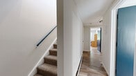 Located in Hartford, CT, this two-floor residential space offers a clean, functional layout designed for comfortable shared living. The interior features light wood-tone flooring throughout, crisp white walls, and an abundance of natural light streaming through large windows that frame views of surrounding greenery.

The open kitchen and living area serves as the heart of the space, boasting vaulted ceilings that lend an airy, expansive feel. The kitchen is equipped with white cabinetry, granite-style countertops, a full-size refrigerator, and an electric range — all finished with contemporary black hardware. The adjoining living area provides a relaxed setting with ample room for seating.

Multiple bedrooms are spread across both floors, each featuring light hardwood-style flooring, large windows with natural views, and baseboard heating. At least one bedroom includes a built-in shelved closet with sliding doors, offering practical storage. The rooms maintain a simple, uncluttered aesthetic well-suited for individual occupancy.

A shared full bathroom features a floating wood-tone vanity, an illuminated LED mirror, a matte black faucet, and a tiled shower-tub combination, delivering a refreshed, modern look. A carpeted staircase with a blue handrail connects the two floors via a clean, well-lit hallway.